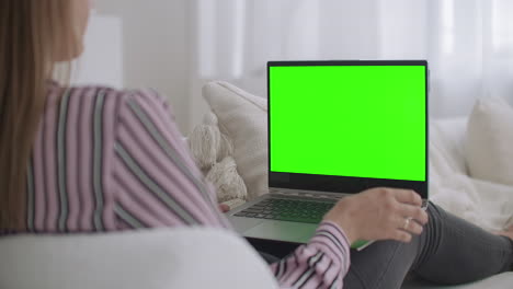 Junge-Frau-Sitzt-Auf-Der-Couch-Und-Hält-Einen-Laptop-Mit-Grünem-Bildschirm-Für-Chroma-Key-Technologie-Und-Chattet-Per-Videoanruf